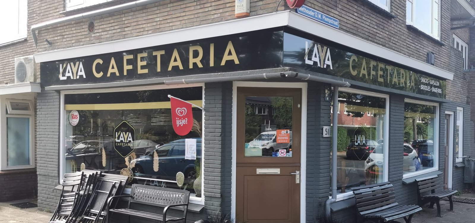 Het hoekpand van Cafetaria Laya aan de Wethouder D.M. Plompstraat 51, met LAYA CAFETARIA in gouden letters op de zwarte luifel.